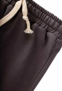 Donkergrijze joggingbroek met een gestructureerd oppervlak, voorzien van een elastische tailleband en een crèmekleurige gevlochten trekkoord.