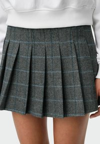 Plisirana suknja od sive tkanine u riblju kost, s plavim kariranim uzorkom i dužinom do sredine bedara, u kombinaciji s bijelim duksericom.