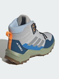 Středně vysoká turistická obuv v šedé a modré barvě, s texturovaným síťovinovým svrškem, gumovou podrážkou, oranžovým detailem a jedinečným vzorem podrážky pro lepší trakci.