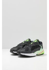 Mustat ja harmaat lenkkarit, joissa on verkkokangasta ja mokkaa, vihreät yksityiskohdat, valkoinen välipohja ja rakenteellinen kumipohja.