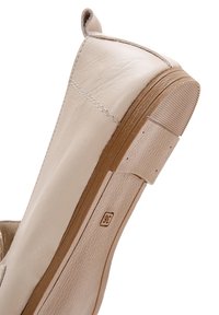Scarpa in pelle beige con forma arrotondata, texture morbida e suola in gomma marrone. Presenta una cucitura e un piccolo manico sul tallone.