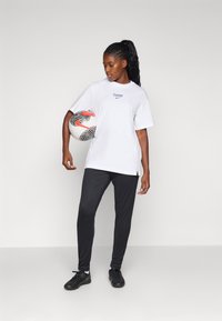 Valkoinen lyhythihainen t-paita, jossa on "PARIS" ja Nike-logo; mustat urheiluhousut; pitää mustaa ja valkoista jalkapalloa, jossa on punaisia yksityiskohtia.