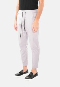 Pantaloni jogger grigio chiaro con cintura elastica e lacci neri; vestibilità affusolata; indossati con scarpe slip-on nere con suole bianche.
