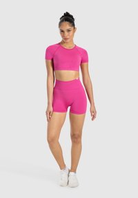 Top corto atletico aderente di un vivace rosa e pantaloni shorts a vita alta, realizzati in un materiale liscio e elastico, progettati per il massimo comfort e mobilità.