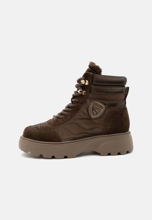 Scarpa da ginnastica alta marrone scuro con suola beige spessa, pannelli trapuntati e in camoscio, colletto imbottito e toppa decorativa sul lato.