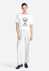 T-shirt bianco cropped con grafica di giraffa, abbinato a pantaloni a palazzo a righe leggere e mocassini neri. Stile semplice, design rilassato.