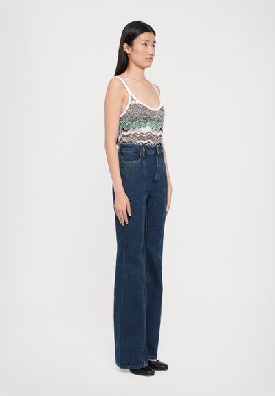 Débardeur court avec un motif zigzag multicolore et un décolleté plongeant, associé à un jean droit taille haute bleu foncé.