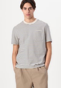Tricou rayé în crem cu dungi orizontale bleumarin, mâneci scurte, decolteu rotund și un buzunar pe piept. Material din bumbac moale.