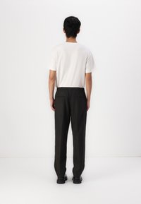 Pantalon noir ample avec taille élastique, poches arrière, porté avec un t-shirt blanc uni à manches courtes, vu de dos.