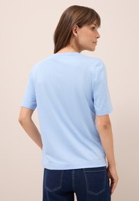 Helles blaues T-Shirt mit kurzen Ärmeln aus weichem Stoff, mit einem klassischen Rundhalsausschnitt und einer lässigen Passform, kombiniert mit dunkelblauen Jeans.