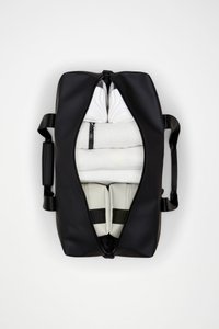 Μαύρη τσάντα τύπου duffel με λεία, ματ υφή, ανοιχτή για να αποκαλύπτει λευκές πετσέτες τυλιγμένες και δύο λευκά αντικείμενα με επένδυση και μαύρα λουριά μέσα.