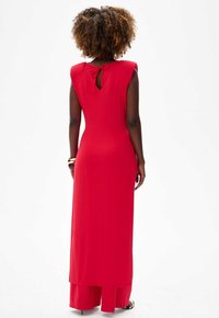 Red maxi dress with a fitted silhouette, capped sleeves, and a keyhole back detail. Smooth fabric with a floor-length cut.