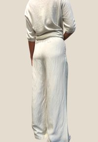 Hvite, lette, vidde bukser med elastisk linning og en glatt, lett rynket tekstur, vist fra baksiden.