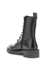 Botín negro de cuero con cremallera lateral, cordones en la parte delantera, tirador y suela de goma gruesa con tacón bajo.