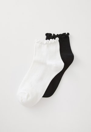 To par ankelsokker med rynkede kanter, en hvid og en sort, placeret ovenpå hinanden på en hvid baggrund.