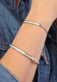 Zilveren armbanden om een pols: de ene glad, de andere met strasstenen. Beide hebben een eigentijds ontwerp en een metalen ketting voor aanpassing.