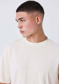 Camiseta de algodón crema con cuello redondo, que presenta un sutil diseño de estrellas en relieve en la parte frontal. Manga corta y corte relajado.