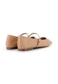 Zapatos planos de color nude con parte superior de cuero suave, diseño de punta elegante y tiras delgadas en el tobillo con detalle de hebilla. Suela plana marrón.