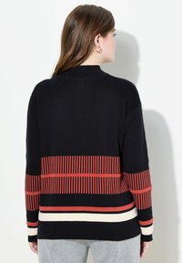 Schwarzer Pullover mit hohem Kragen, mit horizontalen roten und cremefarbenen Streifen. Gerippter Stoff an den Ärmeln und am unteren Saum.