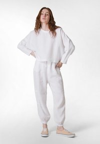 Hvidt linned cropped top med lange ærmer parret med hvide linned joggers. Skoene inkluderer lysebrune sneakers med hvide såler.