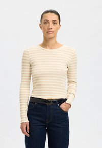 Top de manga comprida às riscas creme e bege, feito de tecido canelado, combinado com jeans azul-escuro e um cinto preto com fivela dourada.