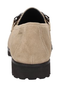 Chaussure en suède beige à bout rond, semelle noire basse et boucle décorative sur les côtés. Surface texturée avec des détails de couture.