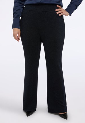 Czarne rozszerzane spodnie o delikatnej fakturze, z elastycznym pasem i błyszczącym wykończeniem, zestawione z czarnymi szpilkami o spiczastym nosku.