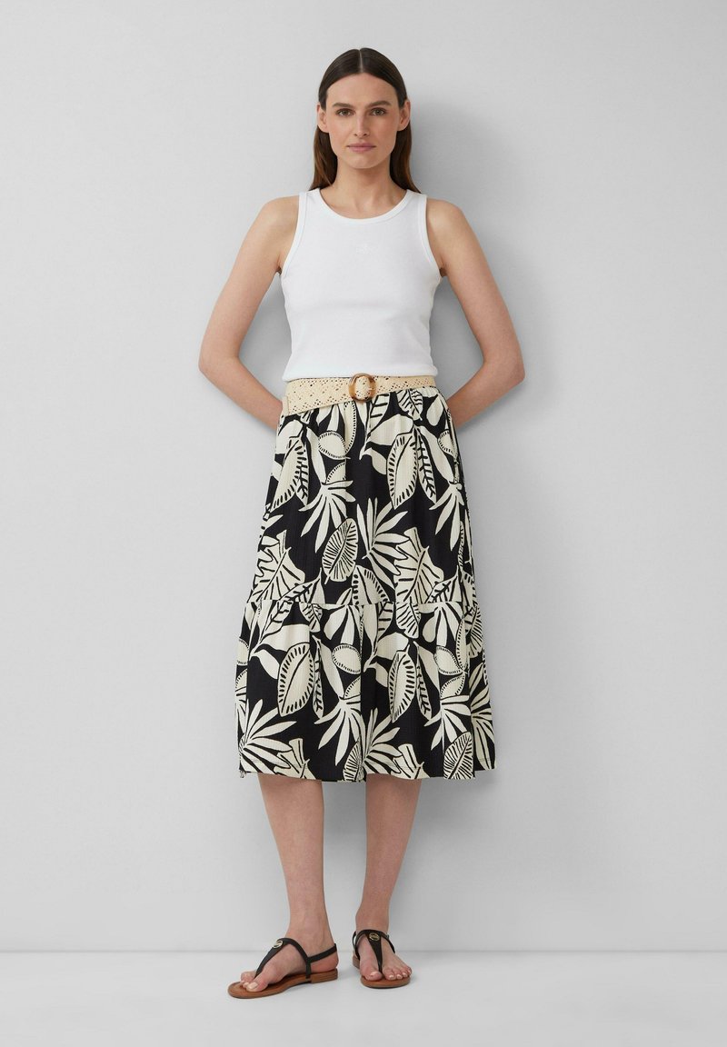 Witte geribbelde tanktop, gecombineerd met een zwarte rok met een beige bladpatroon en een gehaakt beige riem met een ronde gesp. Zwarte sandaal.