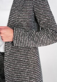 Tkany płaszcz z wzorem pepitki w kolorach czarnym, białym i bordo. Strukturalny krój z szerokimi klapami i teksturowaną tkaniną.