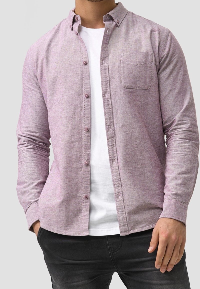 Lys lilla skjorte med knapper, lavet af struktureret stof, med en brystlomme, standart krave og båret over en hvid T-shirt.