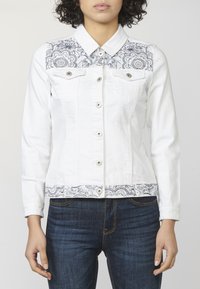 Biała kurtka dżinsowa z niebieskim, haftowanym kwiatowym wzorem na ramionach i dolnym brzegu, z kołnierzem i zapięciem na guziki. Noszone ciemnoniebieskie dżinsy.