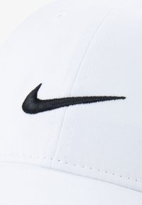 Bela kapa iz bombaža z gladko teksturo. Na sprednji strani ima črno vezeno Nike logo. Klasična zasnova s šestimi paneli.