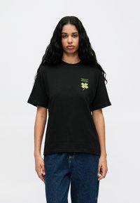 Must rõngaste varrukatega puuvillane T-särk, millel on rohelised tikitud tekstid ja neljaleheline ristikheina disain rindkerel.