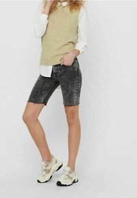 Shorts in denim grigio con orlo grezzo, abbinati a un gilet di maglia beige su una camicia bianca con bottoni e sneakers chunky beige.
