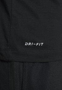 Czarna sportowa koszulka z białym logo "DRI-FIT". Charakteryzuje się gładką teksturą i subtelnymi prążkowanymi detalami przy krawędzi i po bokach.