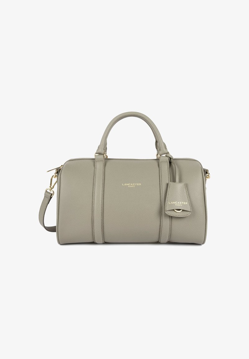 Sac à main cylindrique en cuir gris avec deux poignées, une bandoulière amovible et un logo doré "Lancaster Paris" à l'avant ainsi qu'une étiquette attachée.