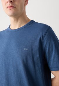 Trumpas rankovės marškinėliai, su apvalia iškirpte, tamsiai mėlynos spalvos, pagaminti iš minkštos medžiagos. Krūtinėje yra subtilus toninis "BOSS" logotipas.