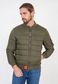 Zielona oliwkowa kurtka puchowa z zamkiem z przodu, ściągaczami przy mankietach i pasie. Posiada haftowane logo oraz pomarańczową metkę na dolnym brzeg. 