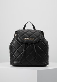 Musta päällystetty nahkainen Valentino-reppu, jossa on läppäkiinnitys, nyöri, ylhäällä oleva kahva ja kultasävyinen brändilogotunnus etuläpällä.