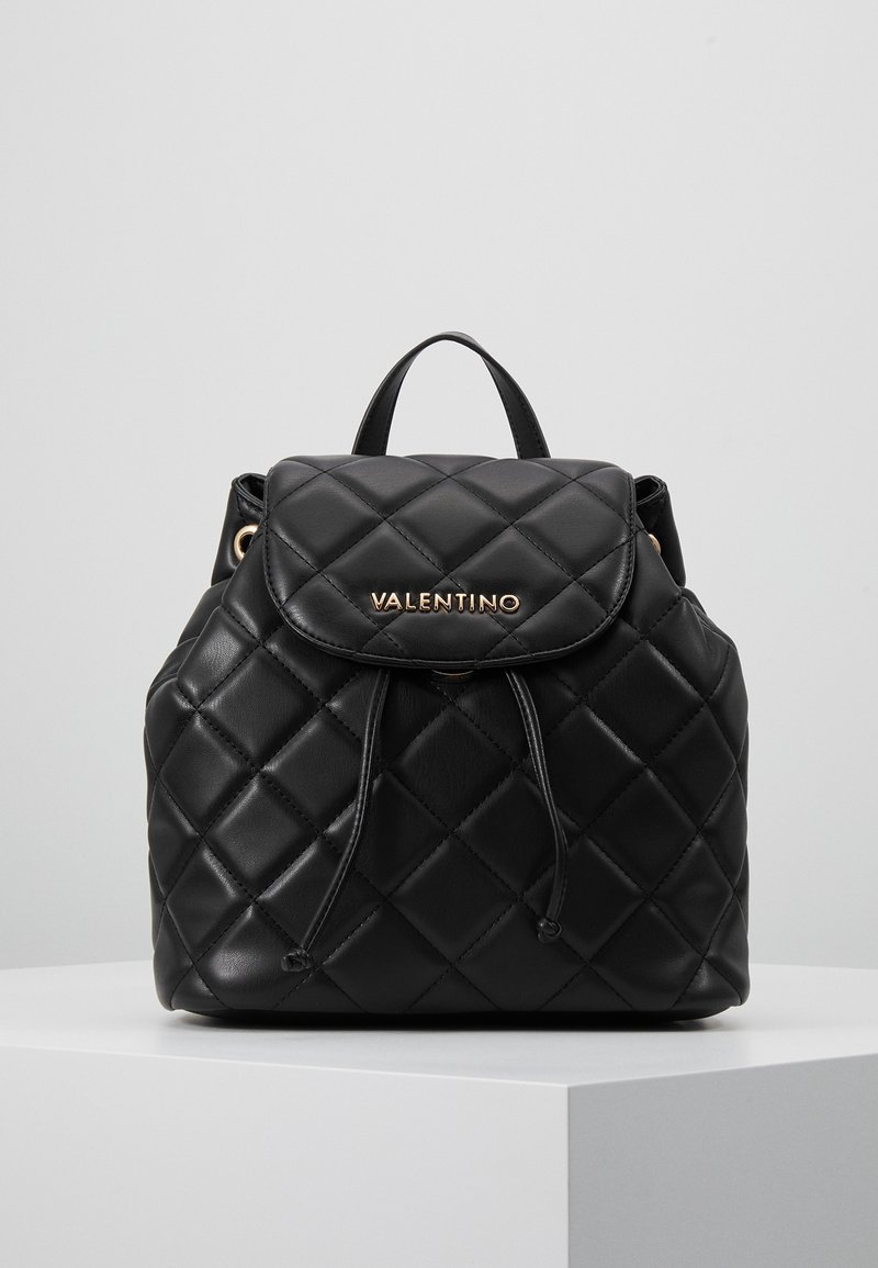 Musta päällystetty nahkainen Valentino-reppu, jossa on läppäkiinnitys, nyöri, ylhäällä oleva kahva ja kultasävyinen brändilogotunnus etuläpällä.