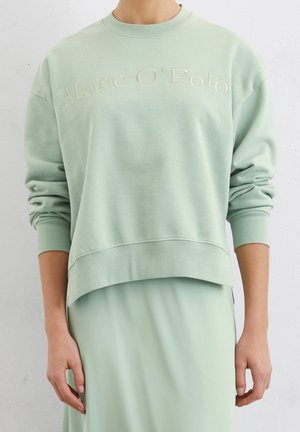 Lichtgroene longsleeve trui met 'Marc O'Polo' geborduurd op de borst, gedragen met een bijpassende lichtgroene rok.
