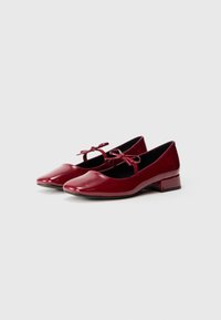 Sapatilhas de balé em verniz vermelho com bico redondo, salto bloco baixo e dois laços decorativos na correia frontal. Acabamento suave e brilhante.