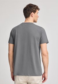 Grå bomullströja med korta ärmar och rundad halsringning, med en slät yta och enkel design, sedd bakifrån.