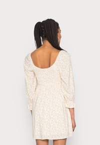 Vestido branco com pequeno padrão floral amarelo, corpete franzido e mangas bufantes. Apresenta um decote nas costas e barra até ao joelho.
