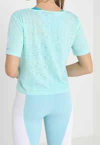 Mintgrön, kortärmad topp med ett strukturerat, något genomskinligt tyg. Har en rund halsringning och kontrasterande kant, som kombineras med ljusblå leggings.