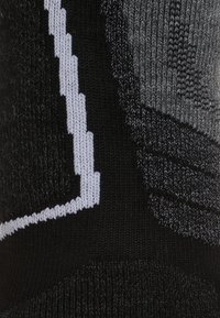 Calcetín de punto en negro y gris con patrones texturizados, un acento en zigzag blanco y una variedad de texturas de puntadas en todo el calcetín.
