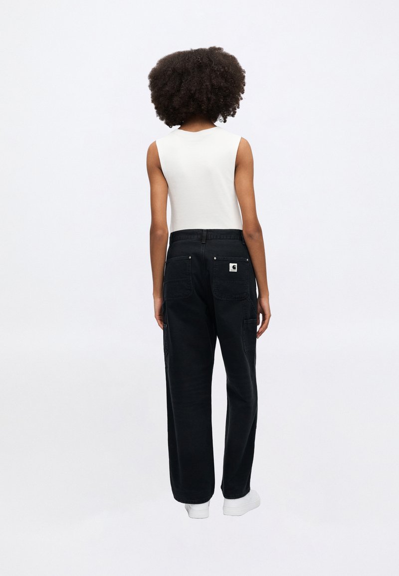 Pantalon cargo noir à coupe décontractée, avec deux poches arrière et une étiquette logo. Associé à un top blanc sans manches ajusté.