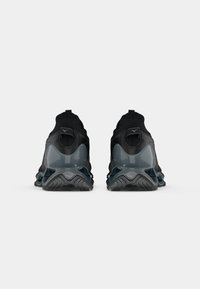 Zapatillas deportivas negras con una parte superior texturizada, una entresuela gris brillante y una suela de goma con diseño, que cuentan con un lazo en la parte posterior.