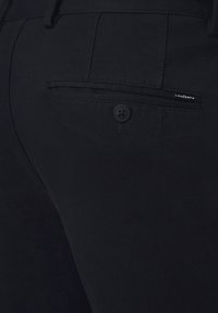 Czarne spodnie z tkaniny o splocie, z tylną kieszenią, z zapięciem na guzik i małą metką marki blisko krawędzi kieszeni. Gładka faktura.