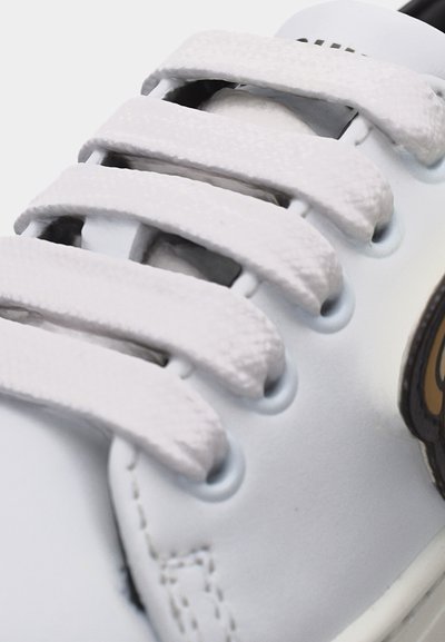 Κοντινό πλάνο λευκού αθλητικού παπουτσιού με φαρδιές, υφασμάτινες λουράκια με βέλκρο που διασταυρώνονται πάνω από το πάνω μέρος του παπουτσιού.